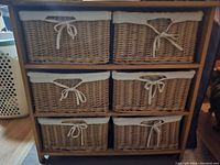 Front view of wooden storage stand holding six rectangular wicker baskets with fabric lining and bows.