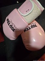 Photo showing front side of pink 10 oz boxing gloves with brand 'ROTTEN' and velcro wrist straps.