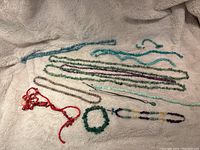 Assorted beaded necklaces and bracelet laid out on cream blanket; includes teal, green, purple, translucent and red coral beads