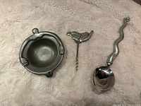 Photo showing three Carrol Boyes signed barware pieces: decorative bowl, bird-shaped corkscrew, wavy handled ladle.