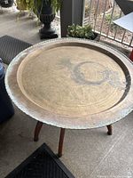 Top view of round brass tabletop showing embossed cultural design and patina.