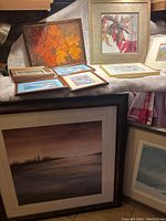 Seven framed art pieces arranged on and around a surface, showing different styles from abstract landscape to floral art.