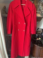Full view of the red wool coat hanging on a hanger, showing front with pockets and buttons.