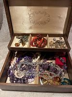 Wooden jewellery box open showing assortment of costume jewelry including bracelets, necklaces, rings, brooches and bone china thimbles in their boxes.