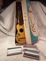 Vintage wooden ukulele with Hawaii design alongside three harmonicas in boxes.