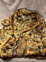 Folded satin-like Natori robe showing floral and leaf print in black and gold on a golden background with black piping trim