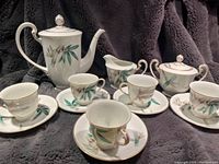 Full view of the Noritake tea set with teapot, 5 cups and saucers, creamer, and lidded sugar bowl arranged on a gray fabric background.