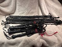 Thirteen braided black leather crops and four whips arranged on a light-colored blanket, showing the braided handles and loops.