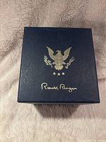 Closed navy blue box with gold Presidential Eagle emblem and Ronald Reagan's signature on the lid.