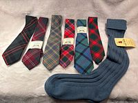 Overview of six tartan wool ties and one pair of blue wool socks laid on a beige surface.