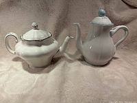 Front view of white porcelain teapot and coffee pot on a soft beige fabric background