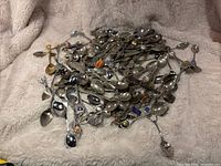 Pile of assorted collectible souvenir spoons showing various designs and colorful enamel emblems on handles.
