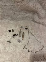 Top-down photo of various small sterling silver pieces including rings, pendants, a chain necklace, cufflinks, and other small jewelry items arranged on a beige fuzzy fabric.