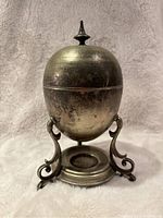 Front view of the silver tone metal egg warmer showing the dome lid with finial and ornate stand