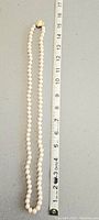 Full length view of the pearl necklace next to a ruler showing approximately 15 inches in length.