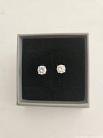 Diamond stud earrings displayed in small grey box with black velvet insert.
