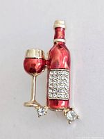 Front view of the red enamel wine bottle and glass brooch with rhinestone accents.