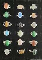 Top view of all 18 fashion rings on black display tray, showing various colored stones and silver-tone bands.