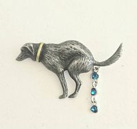 Brooch shaped like a dog with textured metal and a yellow collar, showing the dangling blue gemstone elements on its tail.