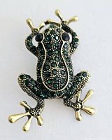 Front view of gold tone frog brooch adorned with green and black rhinestones.