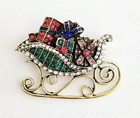 Brooch showing full design of gold-tone metal sleigh decorated with multicolored rhinestones imitating wrapped presents.