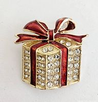 Close-up photo of a Christmas present brooch with clear rhinestones and red enamel bow and ribbons on gold-tone metal.