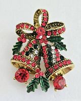 Front view of the rhinestone Christmas bell brooch showing detail of the red bow, two gold-tone bells with multi-colored rhinestones, and green holly leaves with berry accents.