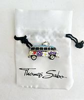 VW Bug Bus charm on Thomas Sabo branded white satin drawstring bag, showing colorful enamel side with peace symbol and 'LOVE' text.