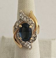 Front view of the vintage 18k HGE cocktail ring showing the blue oval stone surrounded by swirl of white crystals and gold detail.