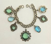 Full view of the bracelet showing six glass charms with blue and green faceted stones on an intricate silver-tone chain.
