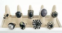 Front view of nine vintage black cocktail rings displayed on fabric ring stand showing variety of black stones, patterns, and silver-tone settings.