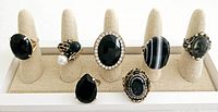 Front view of all nine vintage black cocktail rings arranged on display stand, showing various large black stones including faceted and polished cuts, decorative bands, and rhinestone accents.