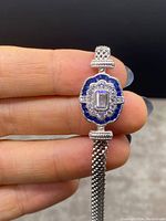 Close-up photo showing the bracelet held by fingers highlighting the central blue and clear stone design.