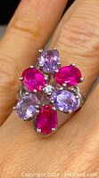 Close-up showing the top and slightly side view of the sterling silver ring with bright pink and light purple stones on a finger.