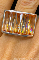 Close-up of the ring on finger highlighting amber-orange faceted gemstones and sterling silver setting.