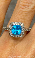 Close-up of the sterling silver ring with cushion-cut blue topaz and surrounding clear stones on finger.