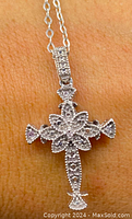 Close-up of sterling silver crucifix pendant showing diamond inlays and detailed design on skin background.