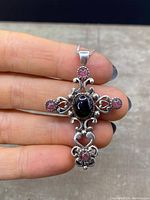 Front view of the sterling silver cross pendant showing the central oval gemstone and four round garnets on each arm of the cross, highlighting the intricate silver filigree and scrollwork design.