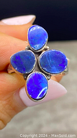 Close-up of sterling silver ring showing four genuine opal stones with deep blue and purple colors, held in hand for scale.