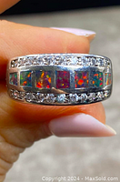 Close-up of ring held between fingers showing inlaid genuine rectangular opals with bright color play and clear stones set above and below.