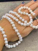 Necklace of genuine white pearls with irregular shapes and a sterling silver clasp, loosely coiled on a hand.