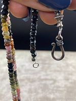 Close-up showing sterling silver hook clasp and small faceted tourmaline beads in black and multicolor.