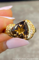Close-up of the ring showing the triangular faceted smokey quartz stone and gold gilt setting with clear stones.