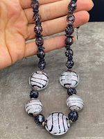 Glass beads of different shapes and sizes, predominantly black with white and red swirls.