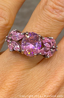 Close-up of the ring with pink stones on finger showing the cluster design with a large round central pink stone and smaller marquise and round stones on sterling silver band.