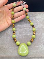 Photo showing full necklace with alternating round tigers eye and olive stone beads, large polished olive green boulder pendant, and sterling silver clasp and accents.