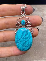 Front view of sterling silver pendant necklace displaying large and small turquoise stones and silver scrollwork.