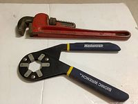 Two wrenches on a white surface: a red 14-inch heavy duty pipe wrench and a Mastercraft Bionic Wrench with black and yellow handles.