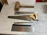 Photo showing four hand saw blades and one wooden mallet on a white surface