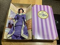 Full view of the boxed doll showing the doll in purple Victorian-style outfit, box with striped design and label.